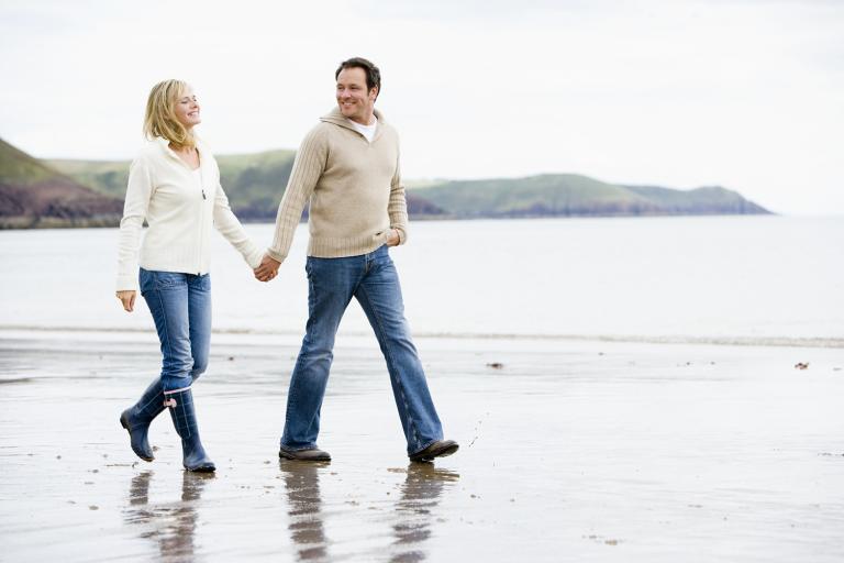 a middle-aged couple holding hands while they walk down a rugged beach